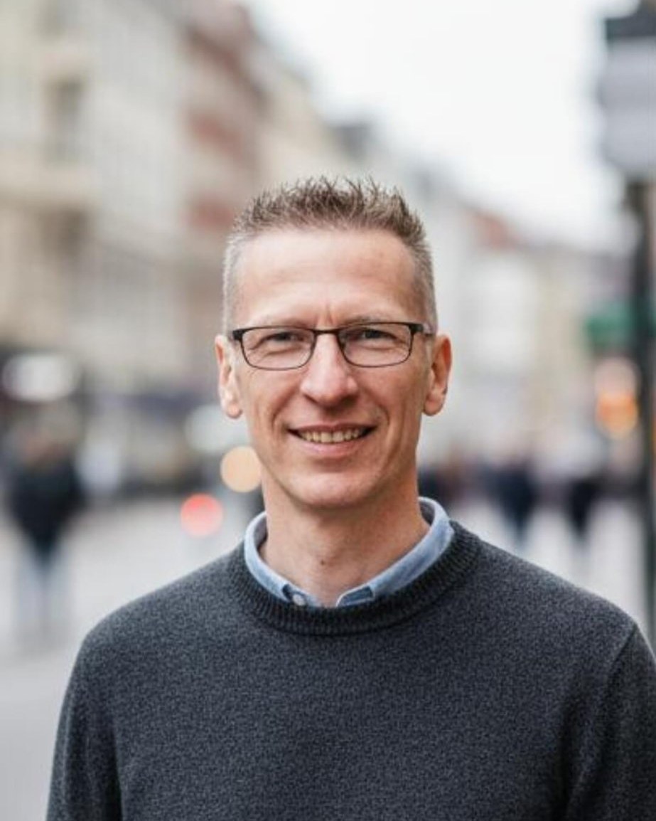 André Dieckmann, Inhaber Immobilien Ratgeber, Porträt in einer Straßenszene, grauer Strickpullover mit hellblauem Hemdkragen.